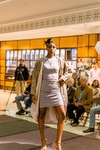 Model Poses on the Runway Wearing a Light Colored Dress and a Beige Coat