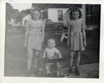 Two Little Girls Standing on Either Side of a Baby in a Push Toy