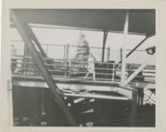 Woman Walking on a Covered Walkway With an Aircraft Carrier Behind It