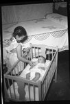 Girl Feeding Baby in Crib by Fred A. Blocker